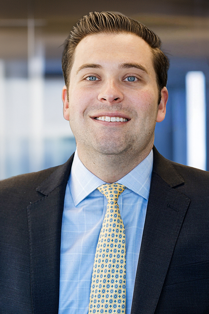Headshot of Brian Harrington smiling with short brown hair, dark blazer, light blue patterned shirt, and a yellow and blue patterned neck tie