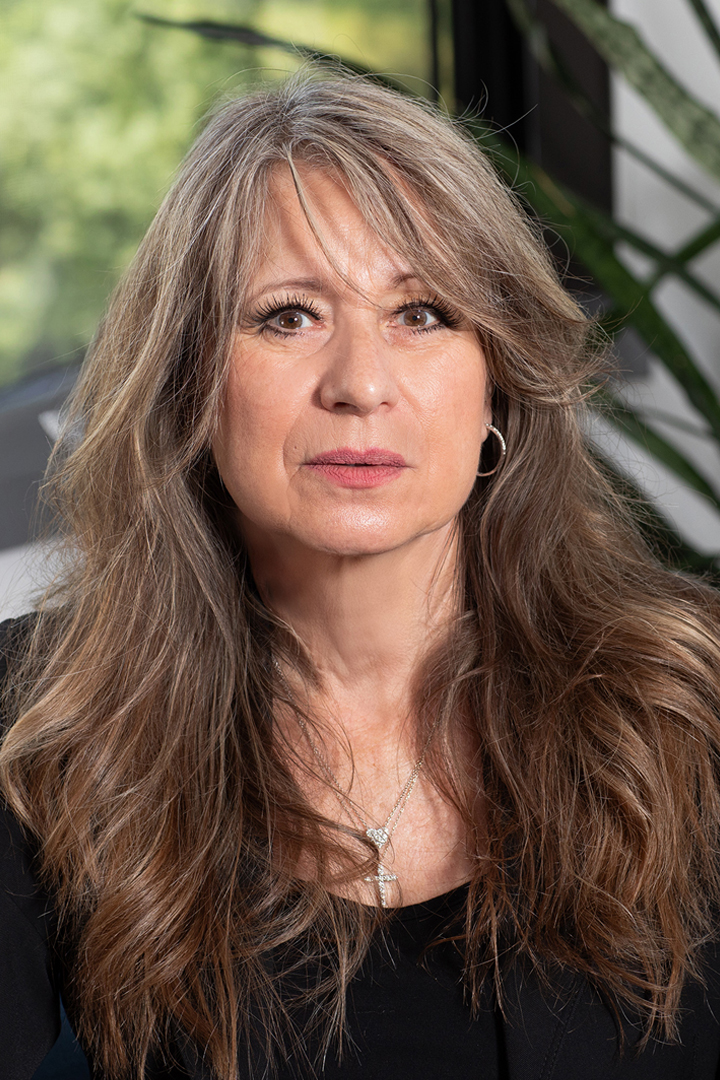 Headshot of woman with long wavy hair wearing a black top and cross necklace
