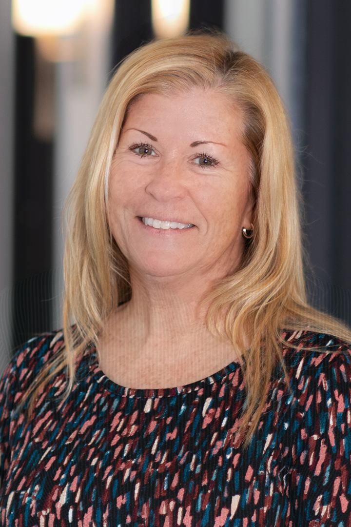 Headshot of Kelly Barrett smiling with long blonde hair and black, blue and pink patterned top