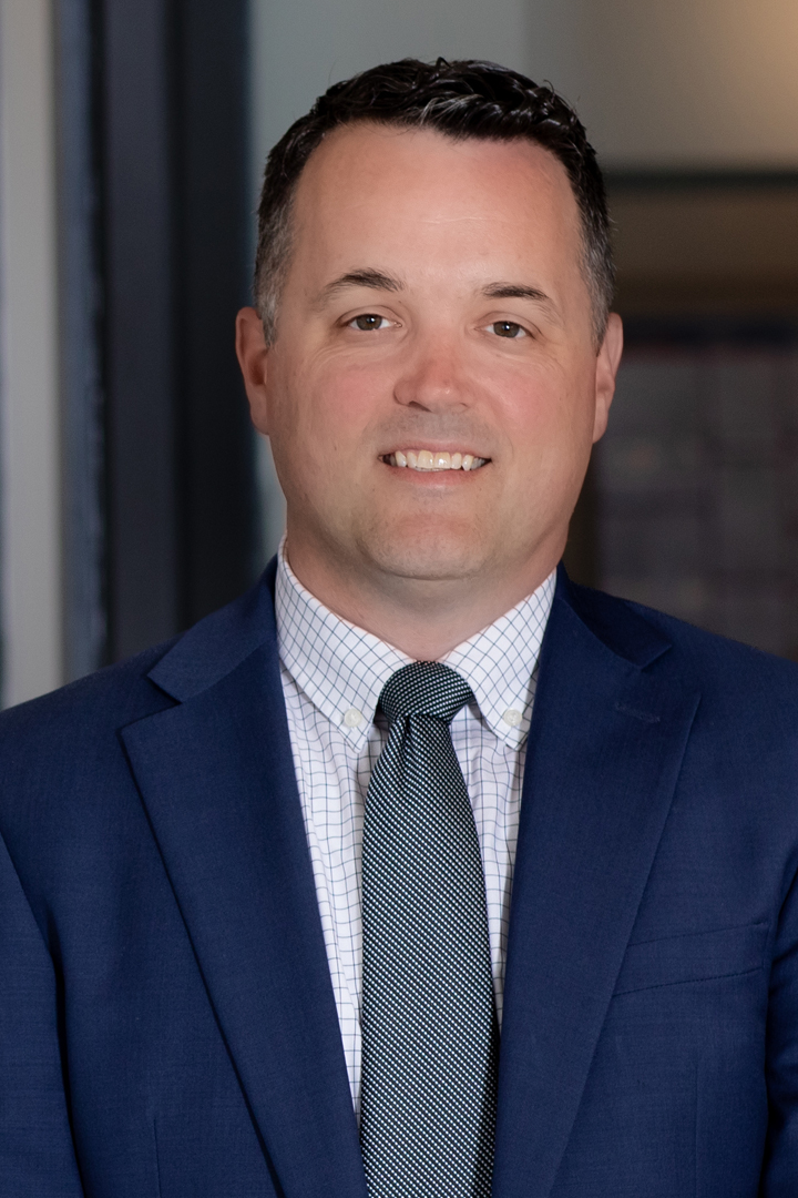 Headshot of Matt Kreiser smiling with short dark hair, dark blue blazer, checked blue and white shirt, with patterned neck tie