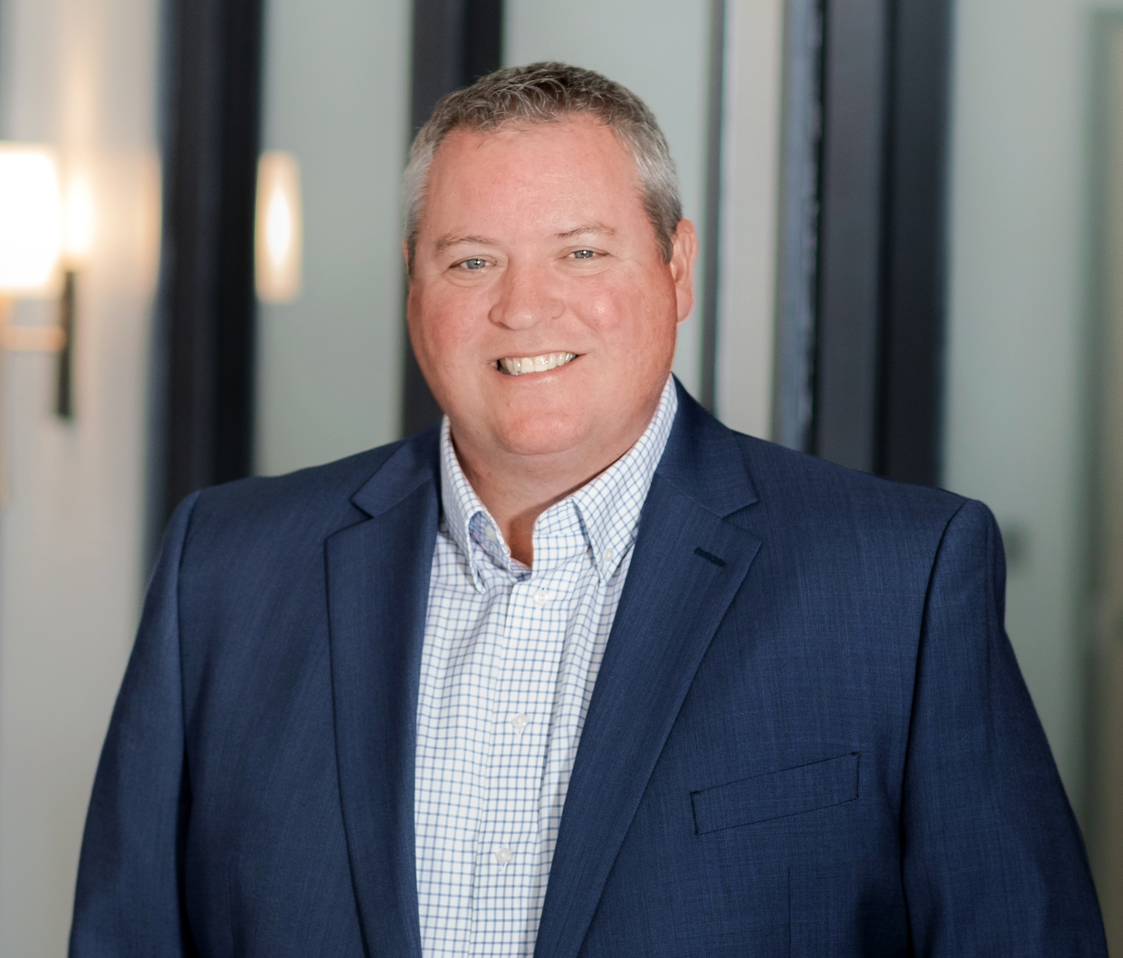 Headshot of Scott Eaton smiling with short hair, blue blazer, and blue and white plaid shirt